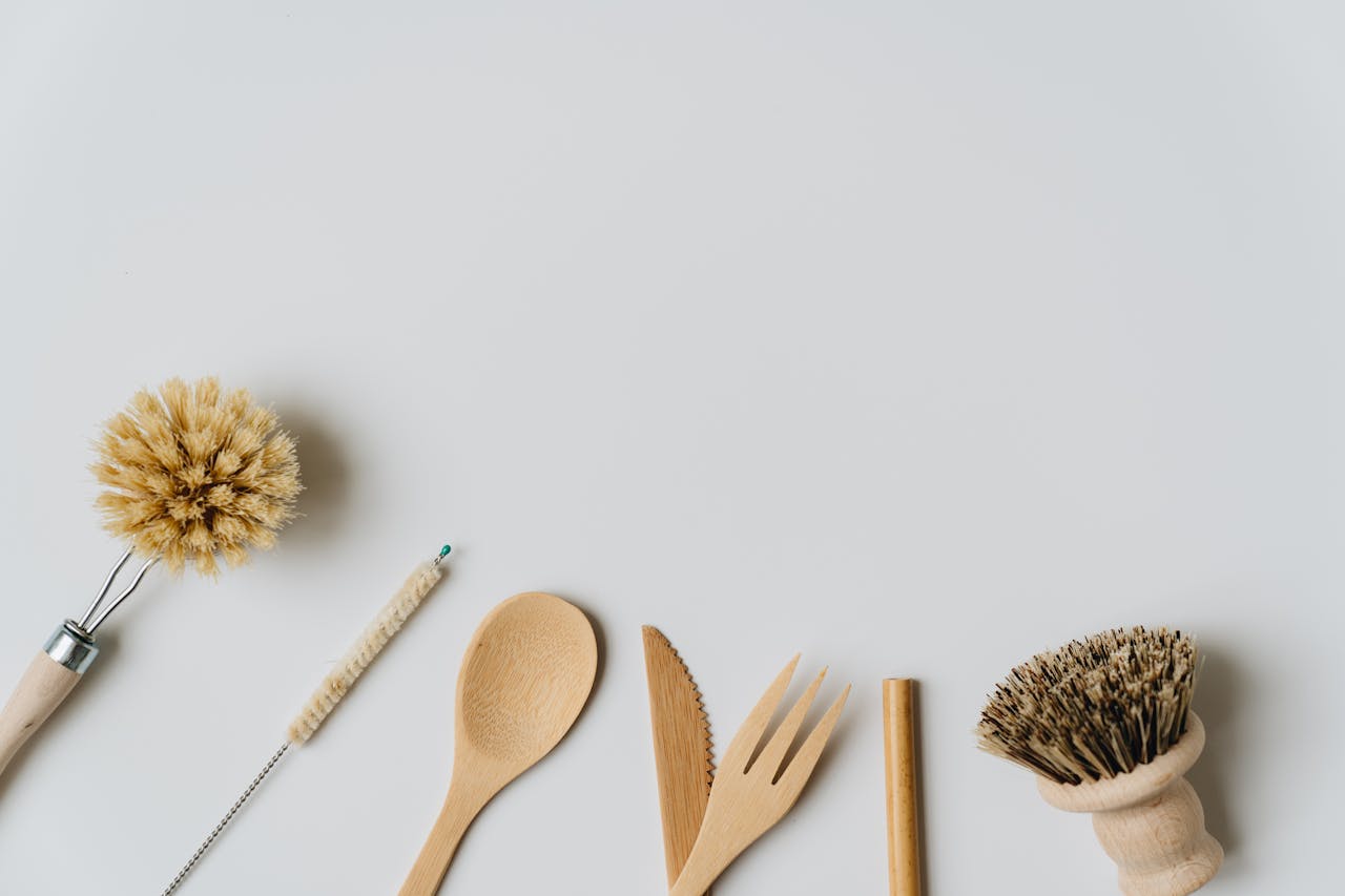 Sustainable wooden kitchen utensils and brushes on a white background, promoting eco-friendly living.