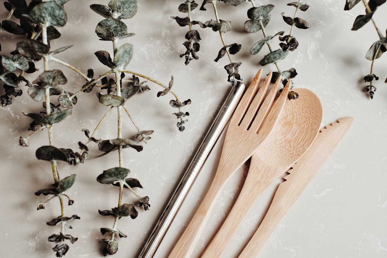 Eco-friendly bamboo cutlery set with eucalyptus leaves on a neutral background.